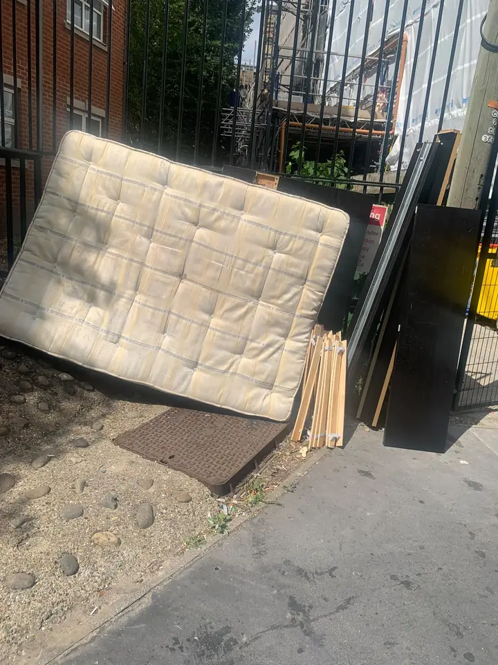 Mattress and furniture panels piled against a metal fence.