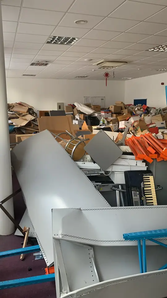 Office interior filled with shelving, furniture, cardboard and loose contents.